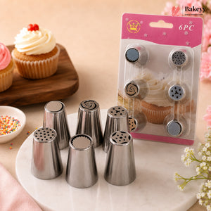Six stainless steel piping nozzles displayed on a white plate, with their pink retail packaging card standing behind them. The scene is styled with cupcakes and sprinkles on a warm beige background, and a 'Bakey' logo appears in the top right corner.