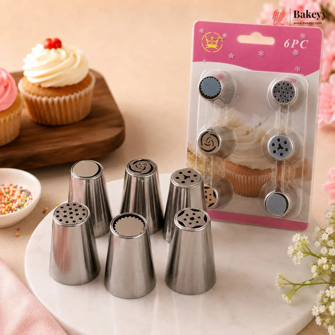 Six stainless steel piping nozzles displayed on a white plate, with their pink retail packaging card standing behind them. The scene is styled with cupcakes and sprinkles on a warm beige background, and a 'Bakey' logo appears in the top right corner.
