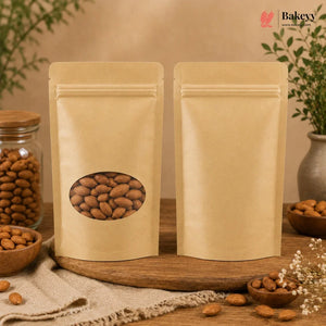 Two blank kraft paper stand-up pouches with one featuring an oval window showing almonds, displayed on a wooden board with almonds and a glass jar of almonds in a styled setting. The Bakey logo is visible in the top right corner.