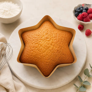 Star-shaped cake on a white plate with berries and a whisk in the background