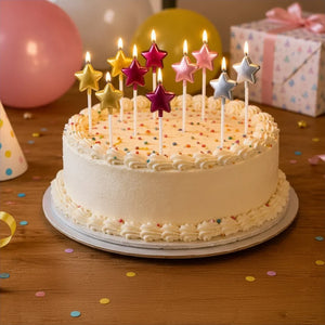 Birthday cake with star-shaped candles on a wooden table with balloons and a gift box in the background.