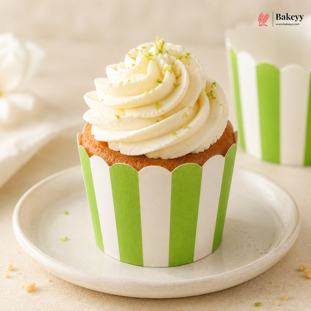 Cupcake with white frosting and green sprinkles on a green and white striped wrapper, placed on a white plate.