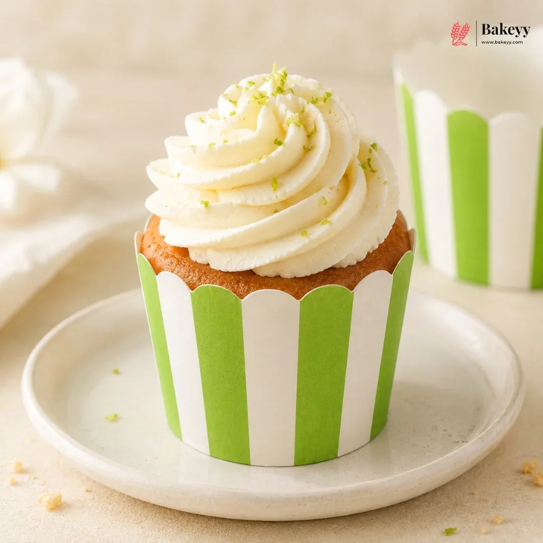 Cupcake with white frosting and green sprinkles on a green and white striped wrapper, placed on a white plate.