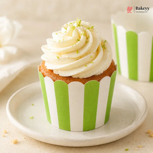 Cupcake with white frosting and green sprinkles on a green and white striped wrapper, placed on a white plate.