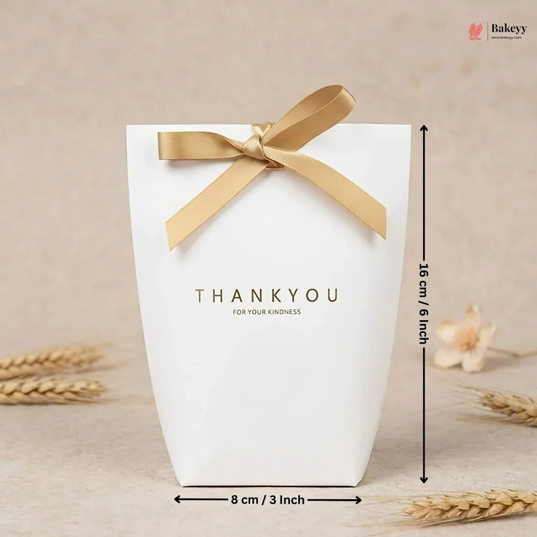 White gift box with gold ribbon and 'THANKYOU' text, placed on a beige surface with wheat stalks.