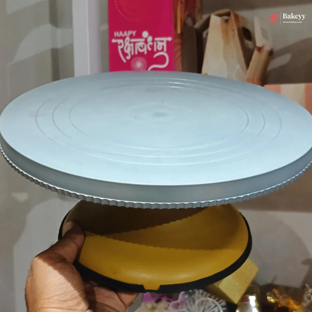 Hand holding a yellow cake stand with a blue circular object on top, against a blurred background.