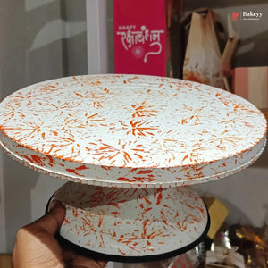 Two-tiered cake stand with orange and white pattern held by a hand, with a blurred background.