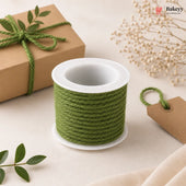 Spool of green twine on a white surface with a gift box and decorative elements.