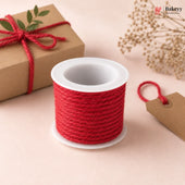 Spool of red twine on a white surface with a gift box and tag in the background.