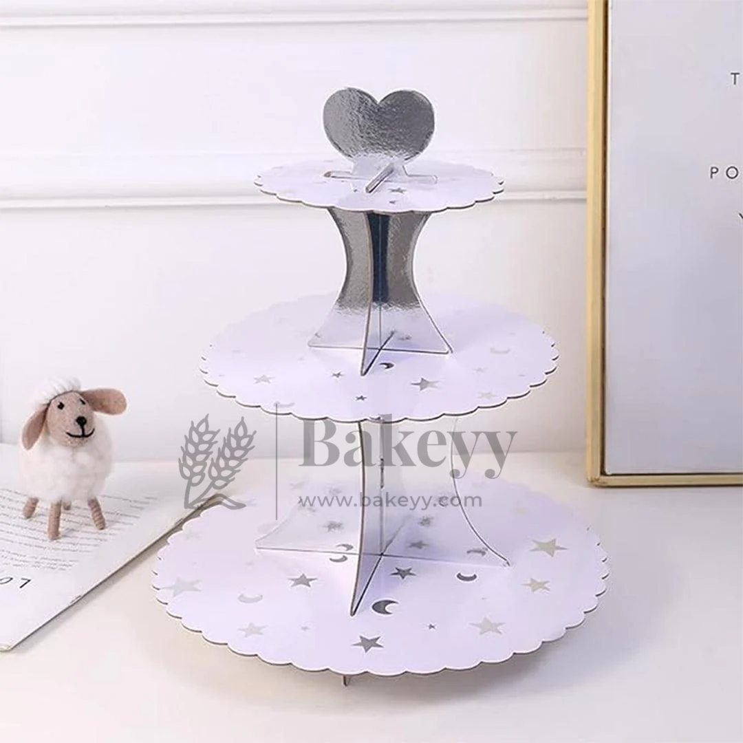 Three-tiered white cake stand with decorative cutouts on a light surface, branded 'Bakeyy'.