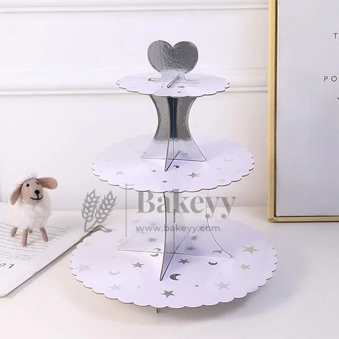 Three-tiered white cake stand with decorative cutouts on a light surface, branded 'Bakeyy'.