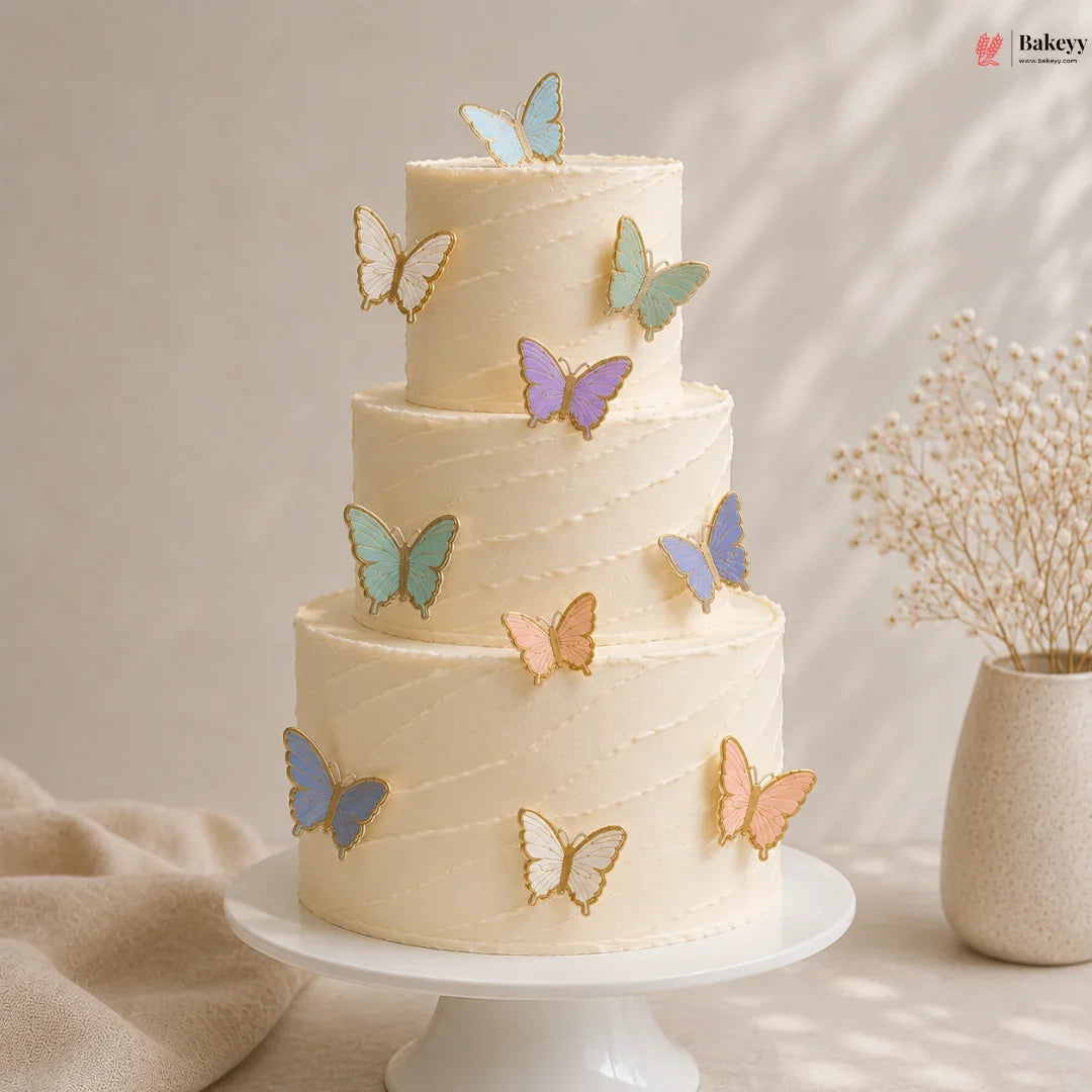 Three-tiered cake with butterfly decorations on a white cake stand, with a vase of dried flowers in the background.