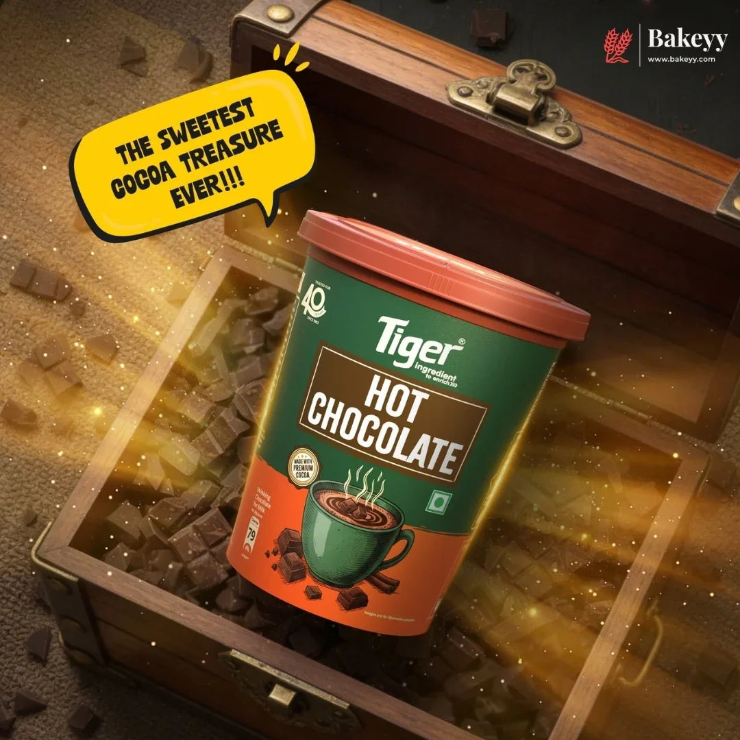 A container of Tiger Brand Hot Chocolate placed inside an open wooden treasure chest filled with chocolate pieces and glowing gold sparkles. A yellow speech bubble reads 'THE SWEETEST COCOA TREASURE EVER!!!' and the Bakeey website logo appears in the top right corner.