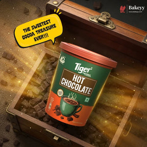 A container of Tiger Brand Hot Chocolate placed inside an open wooden treasure chest filled with chocolate pieces and glowing gold sparkles. A yellow speech bubble reads 'THE SWEETEST COCOA TREASURE EVER!!!' and the Bakeey website logo appears in the top right corner.