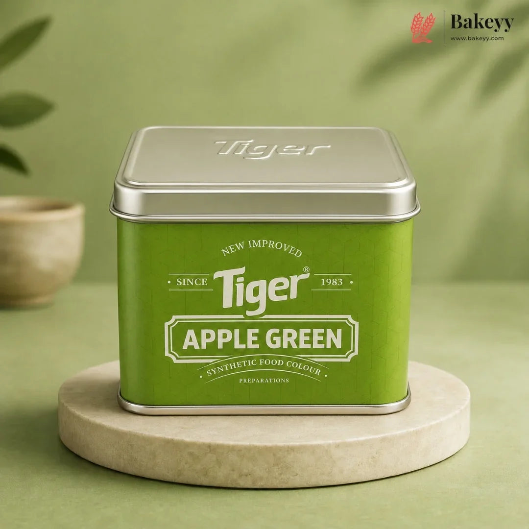 A square green tin of Tiger Apple Green synthetic food colour, displayed on a round beige stone coaster against a soft green background.