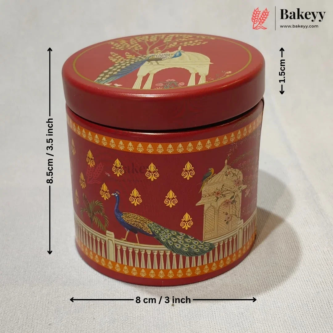 A red cylindrical metal cake tin with a lid, decorated with gold and multicolor peacock and architectural motifs. Black dimension arrows and text indicate a height of 8.