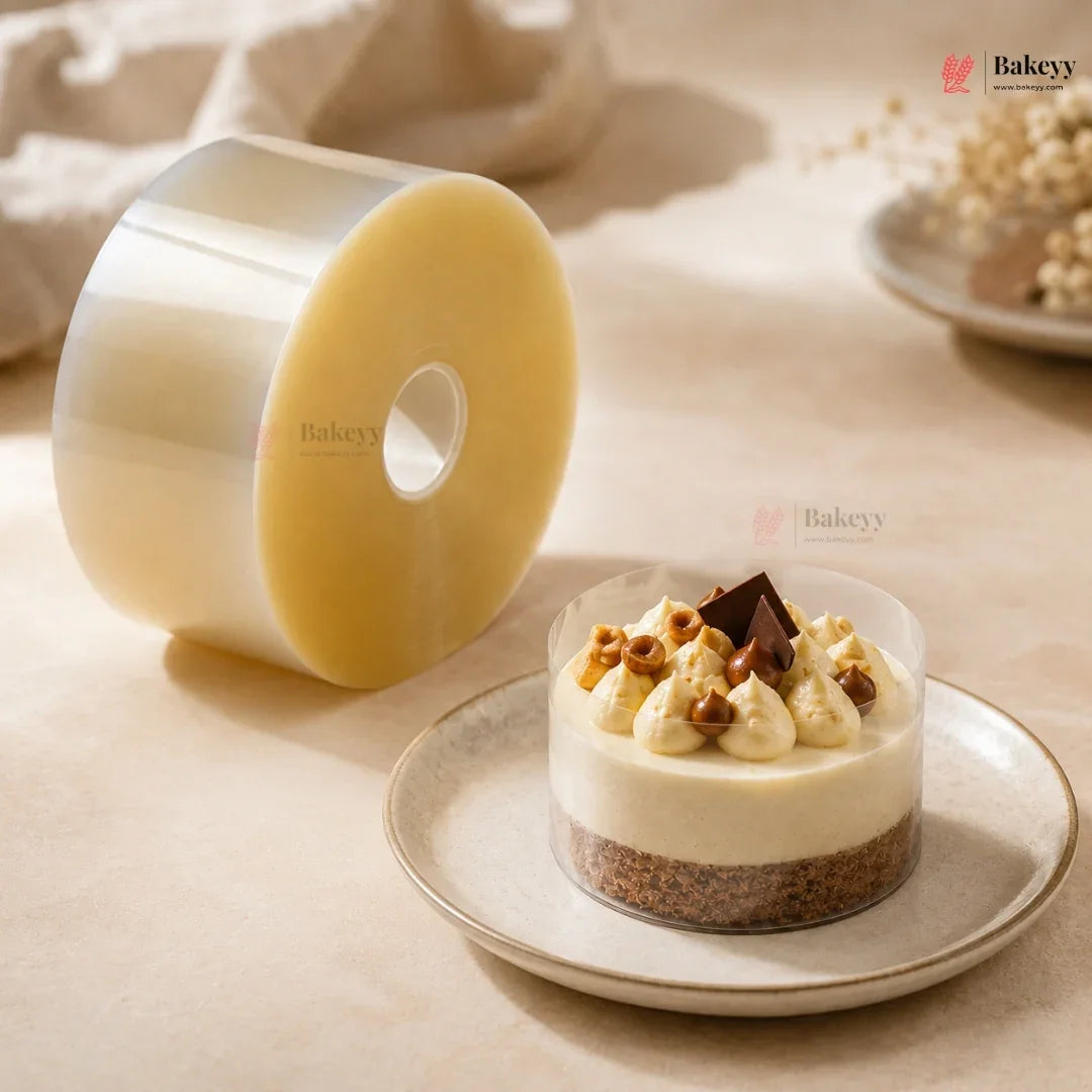 A roll of clear plastic wrap with a pale yellow backing is shown beside a small dessert cup on a plate, styled on a warm beige surface with soft background props. The Bakeey brand name appears in the top right and faintly on the product roll.