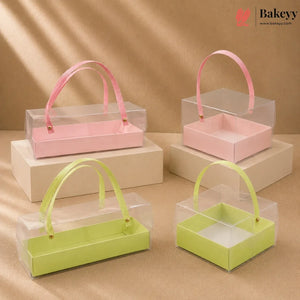 Clear gift boxes with pink and green handles on beige platforms, featuring the Bakeyy brand.