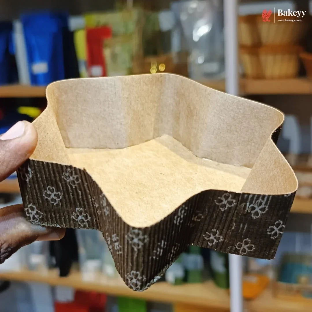 Hand holding a square cardboard cake pan with decorative edge in a kitchen setting.