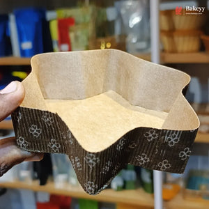 Hand holding a square cardboard cake pan with decorative edge in a kitchen setting.
