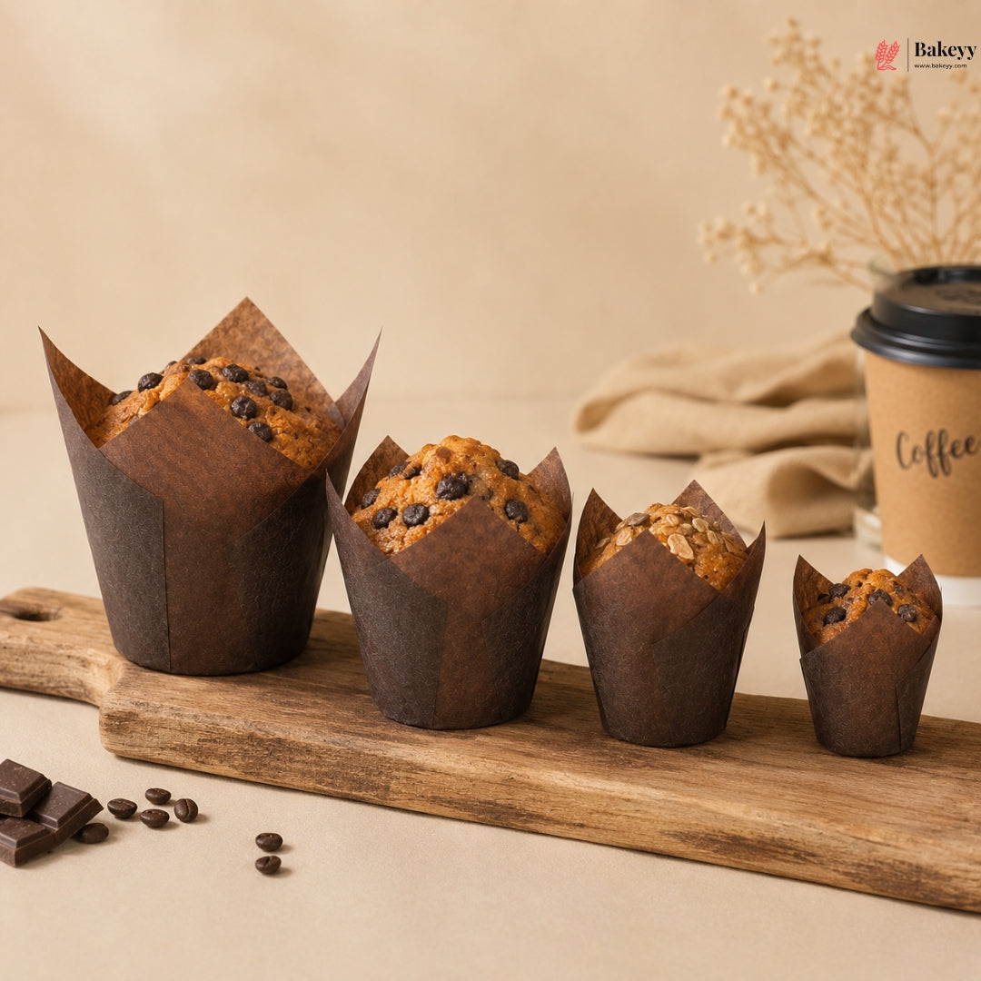 Chocolate muffins in brown paper cups on a wooden board with a coffee cup in the background.