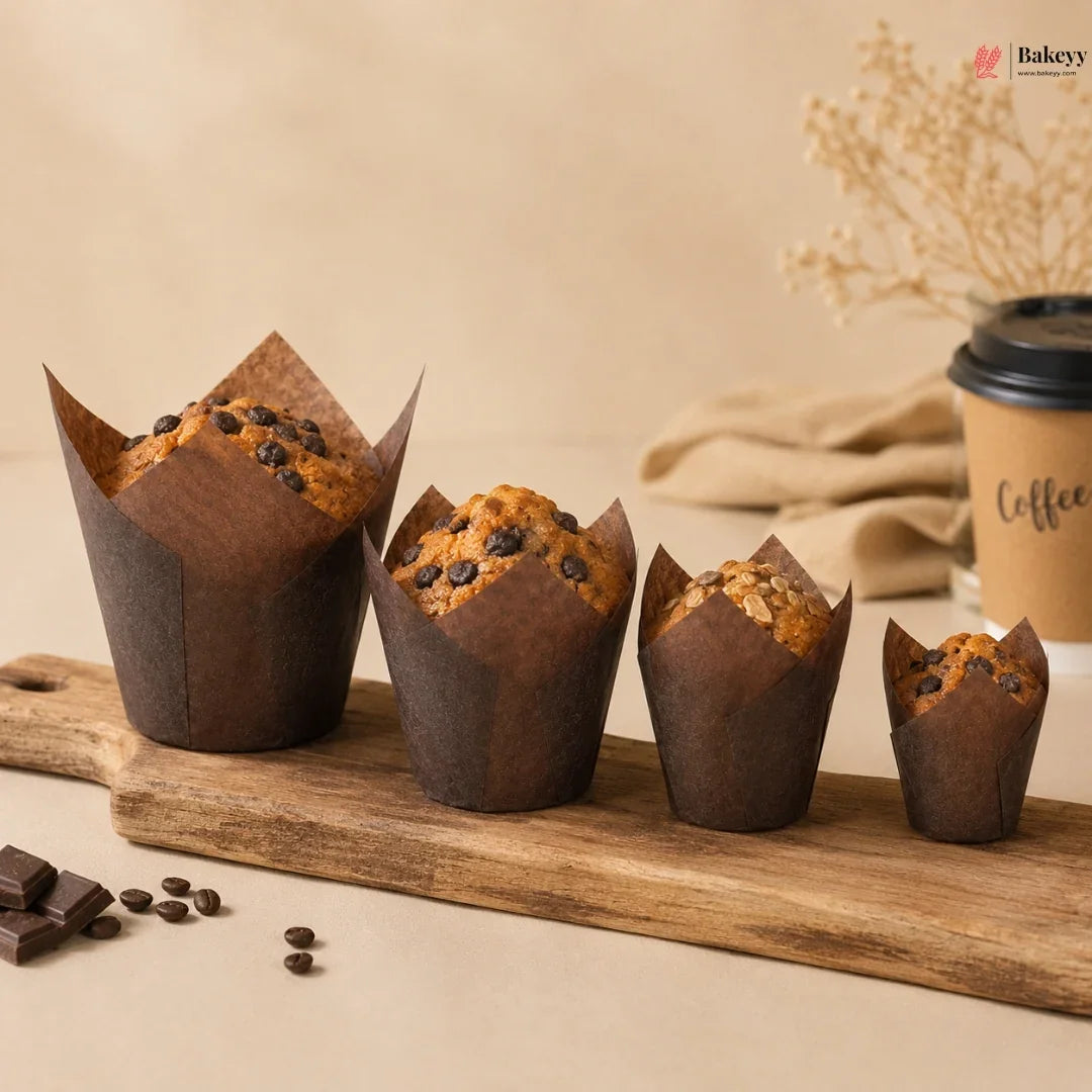 Chocolate muffins in brown paper cups on a wooden board with a coffee cup in the background.