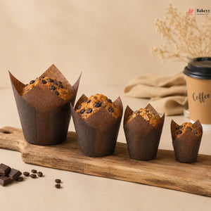 Chocolate muffins in brown paper cups on a wooden board with a coffee cup in the background.