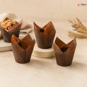 Three brown tulip-shaped muffin cups on a light surface with a blurred background.