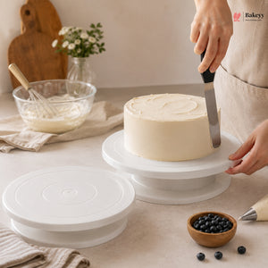 Person frosting a cake on a white cake stand with a spatula, surrounded by baking tools and ingredients.