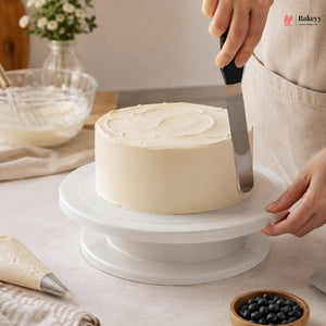 Person frosting a cake on a white turntable with a spatula