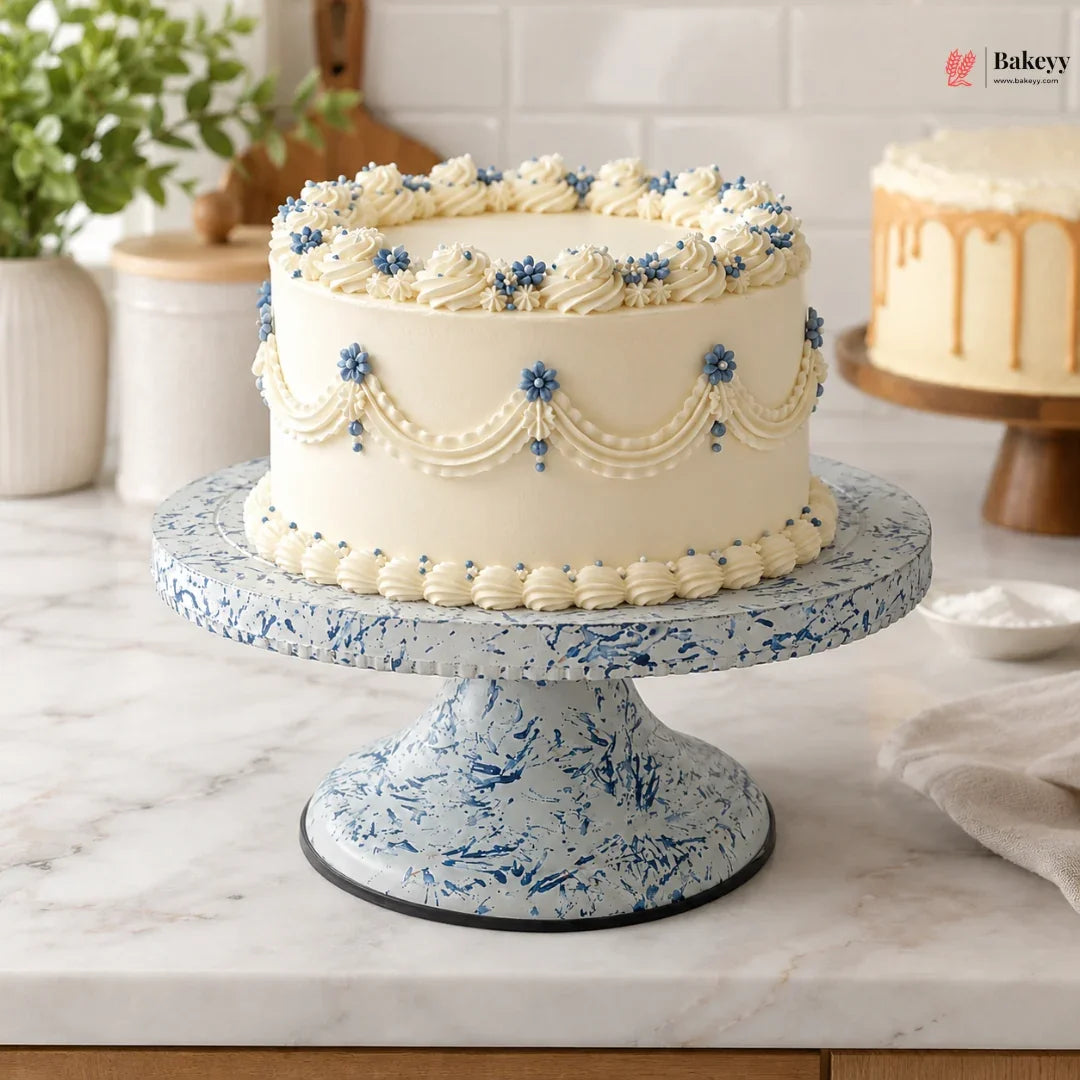 Decorative cake on a blue speckled cake stand with a kitchen setting in the background.