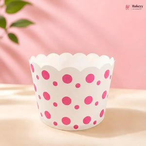 A white paper cupcake liner with pink polka dots, displayed on a light beige surface against a soft pink background with a leafy green accent in the upper left.