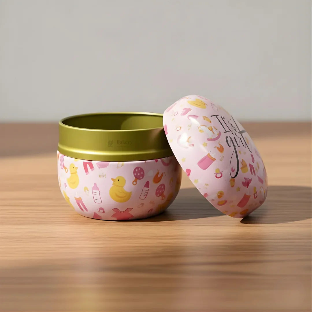 Pink round hamper tin box with baby girl-themed designs, open on wooden table, Bakeyy gift packaging