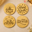 Four round gold-colored Diwali-themed engraved coasters or placemats arranged in a 2x2 grid on a beige surface. The designs include a diya, stars, fireworks, and the words 'Happy Diwali' in dark brown lettering.