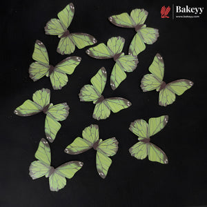 Ten butterfly-shaped cake toppers in light green with dark purple veins and tips, arranged on a black background. The Bakeey brand logo is visible in the top right corner.