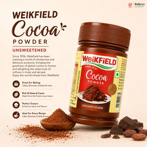 A bottle of Weikfield Unsweetened Cocoa Powder shown on a warm beige background with decorative cocoa powder, chocolate pieces, and text describing the product. The Weikfield brand logo is clearly visible on the bottle and in the top right corner.