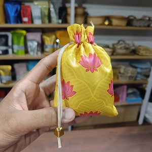 Yellow drawstring bag with pink floral patterns held by a hand in a store setting.