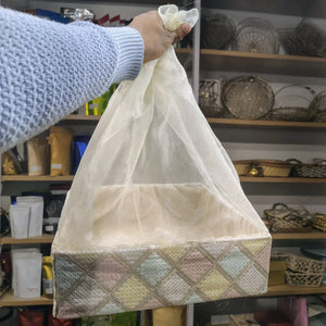 Hand holding a patterned box with a sheer white cover against a background of shelves with various items.