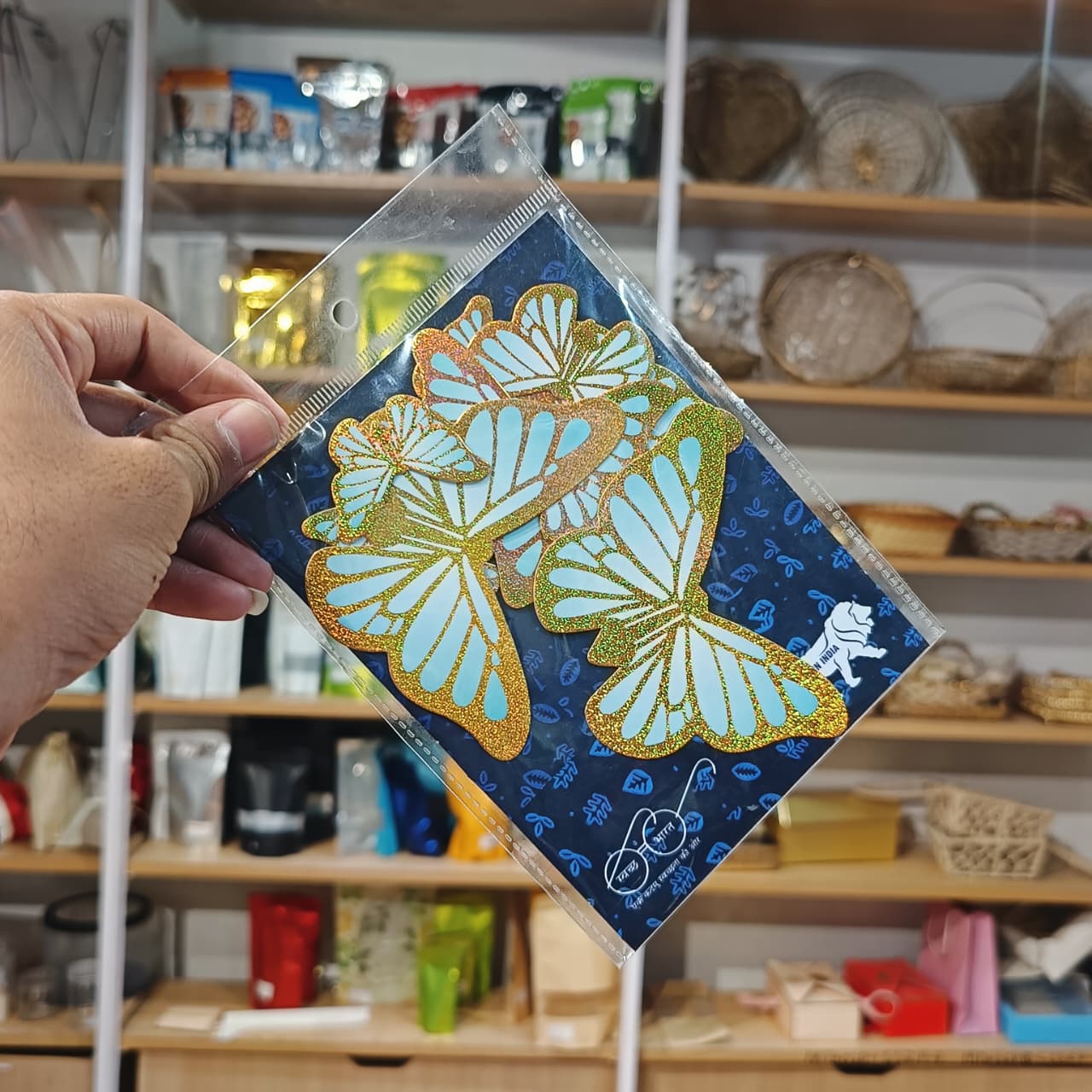 Hand holding a decorative card with butterfly design in front of a store shelf.