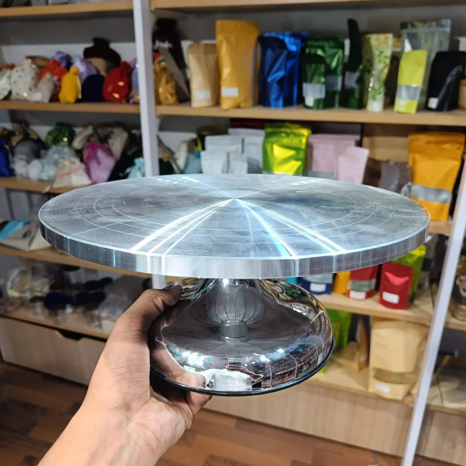 Metallic cake stand held in front of a shelf with various items