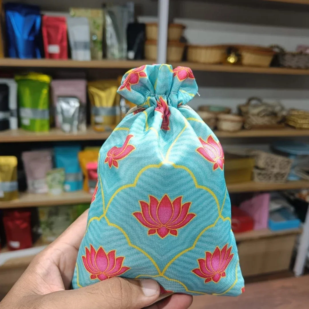 Hand holding a blue drawstring bag with pink lotus patterns in front of shelves with various items.