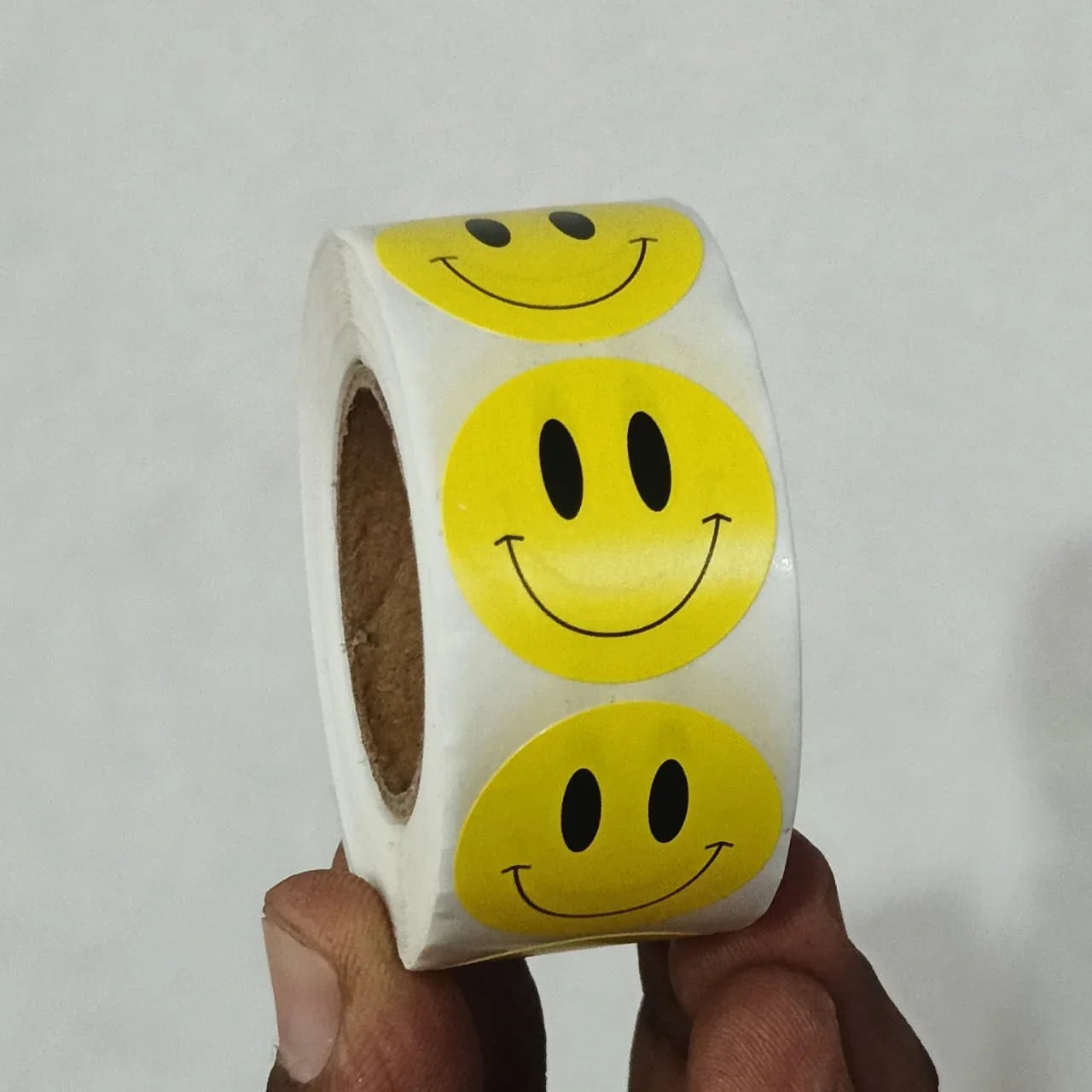Roll of yellow smiley face stickers held by a hand against a white background