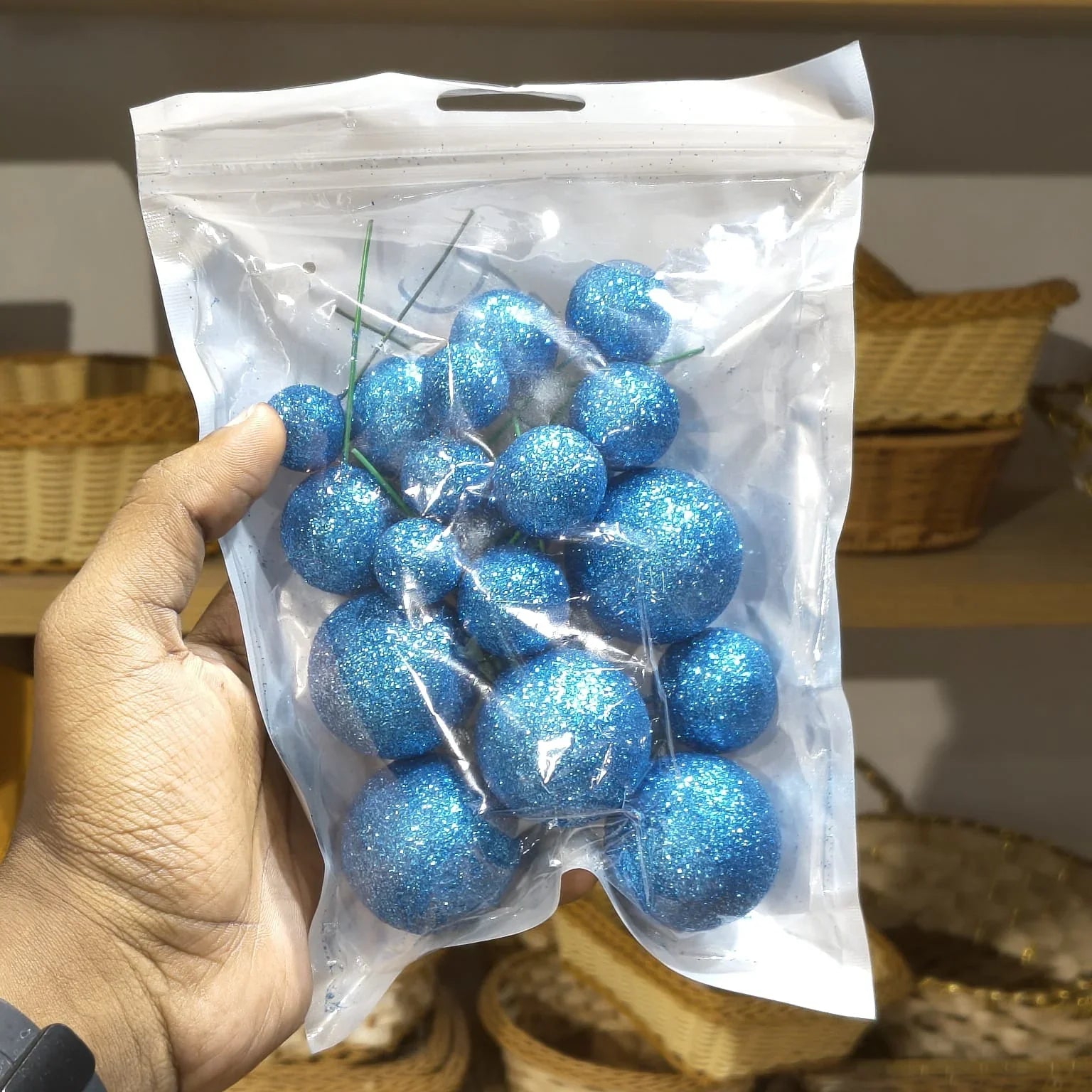 Hand holding a clear plastic bag with blue glittery balls against a neutral background