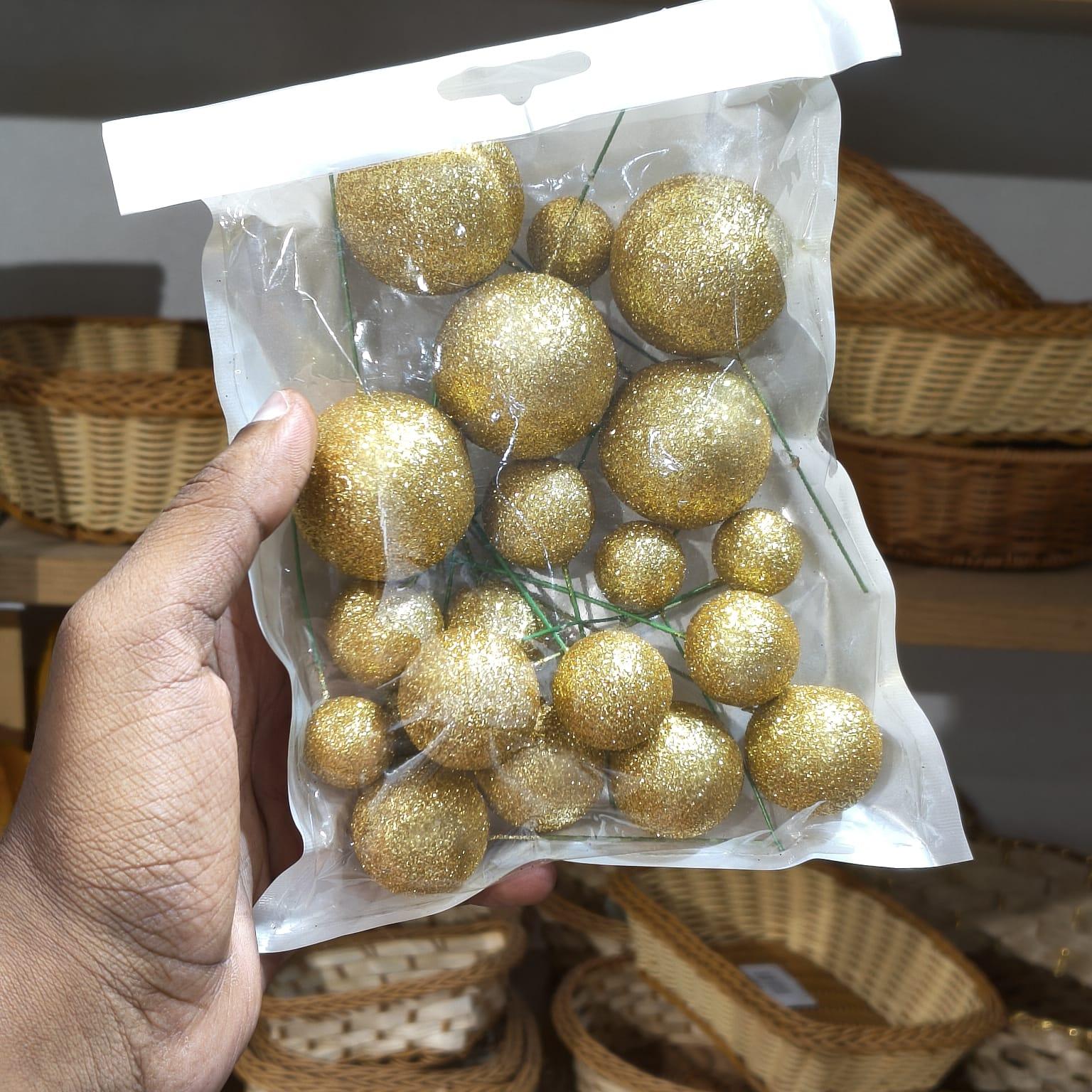 Gold glittery balls in a clear plastic bag held by a hand with wicker baskets in the background.