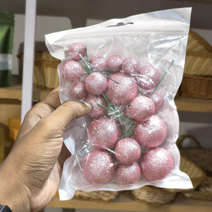 Hand holding a clear plastic bag with pink glittery balls against a blurred indoor background