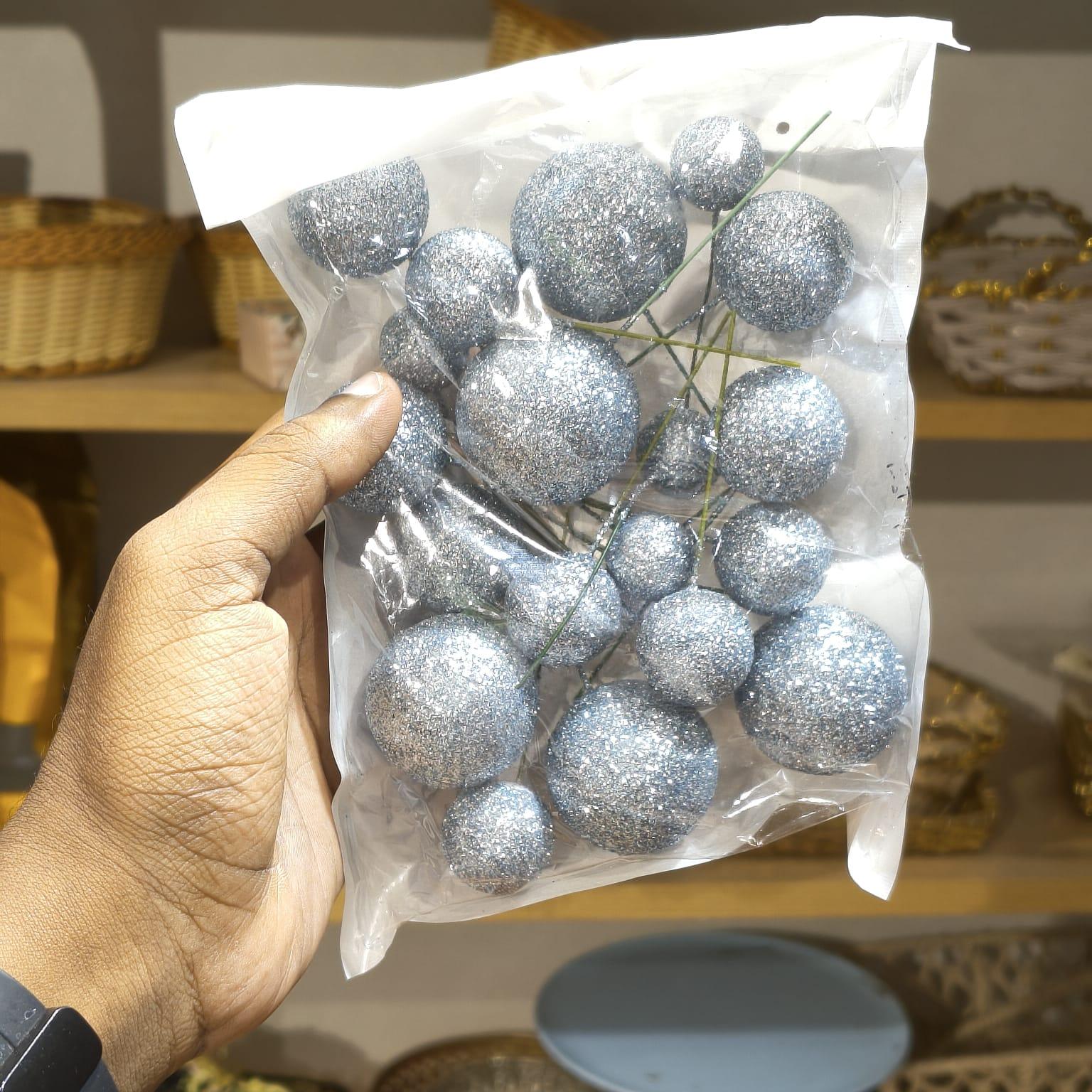 Hand holding a clear plastic bag with silver glittery balls against a blurred background