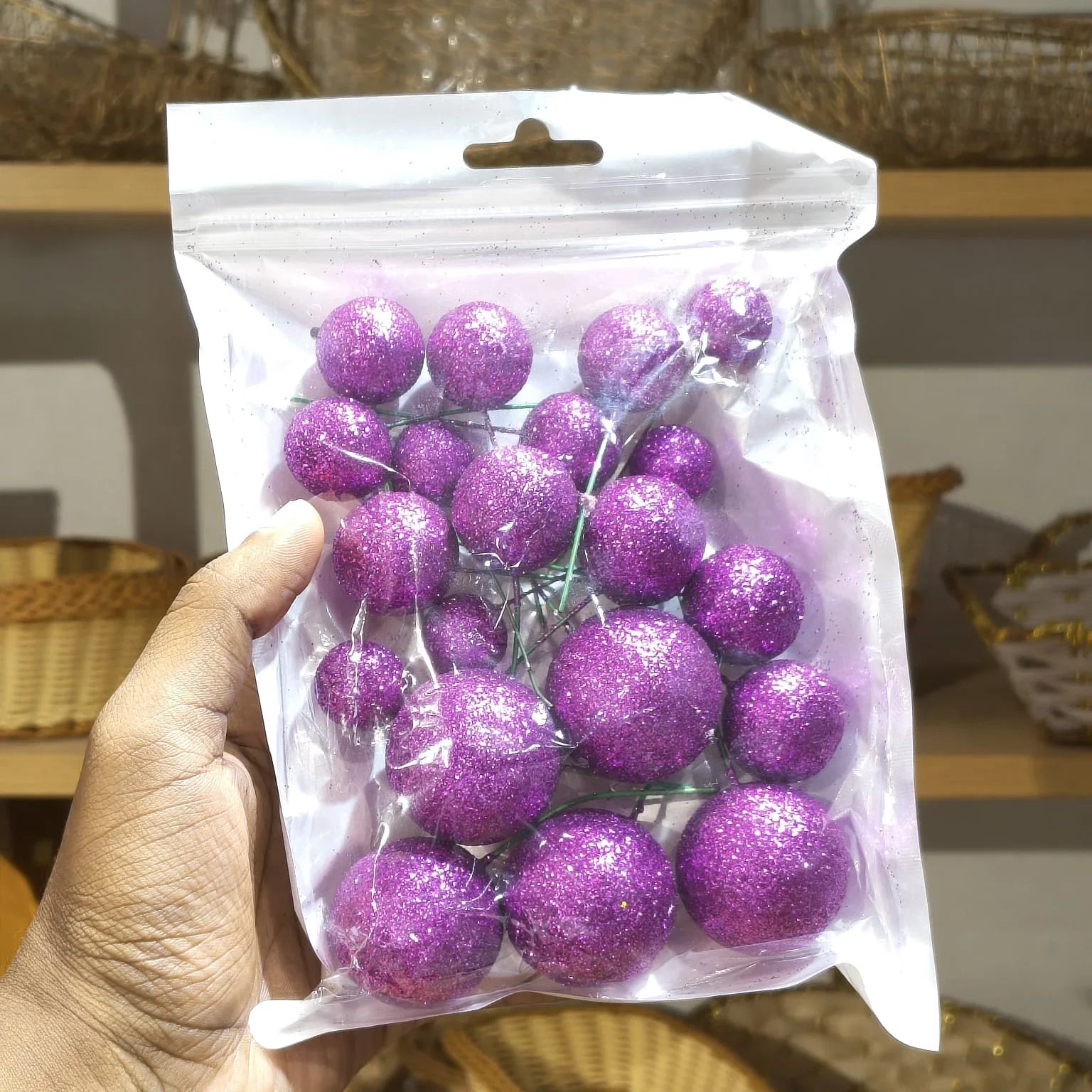 Hand holding a clear plastic bag with purple glittery balls.