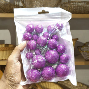 Hand holding a clear plastic bag with purple glittery balls.