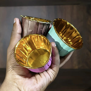 Hand holding two small, colorful foil cups with a gold interior against a wooden background.