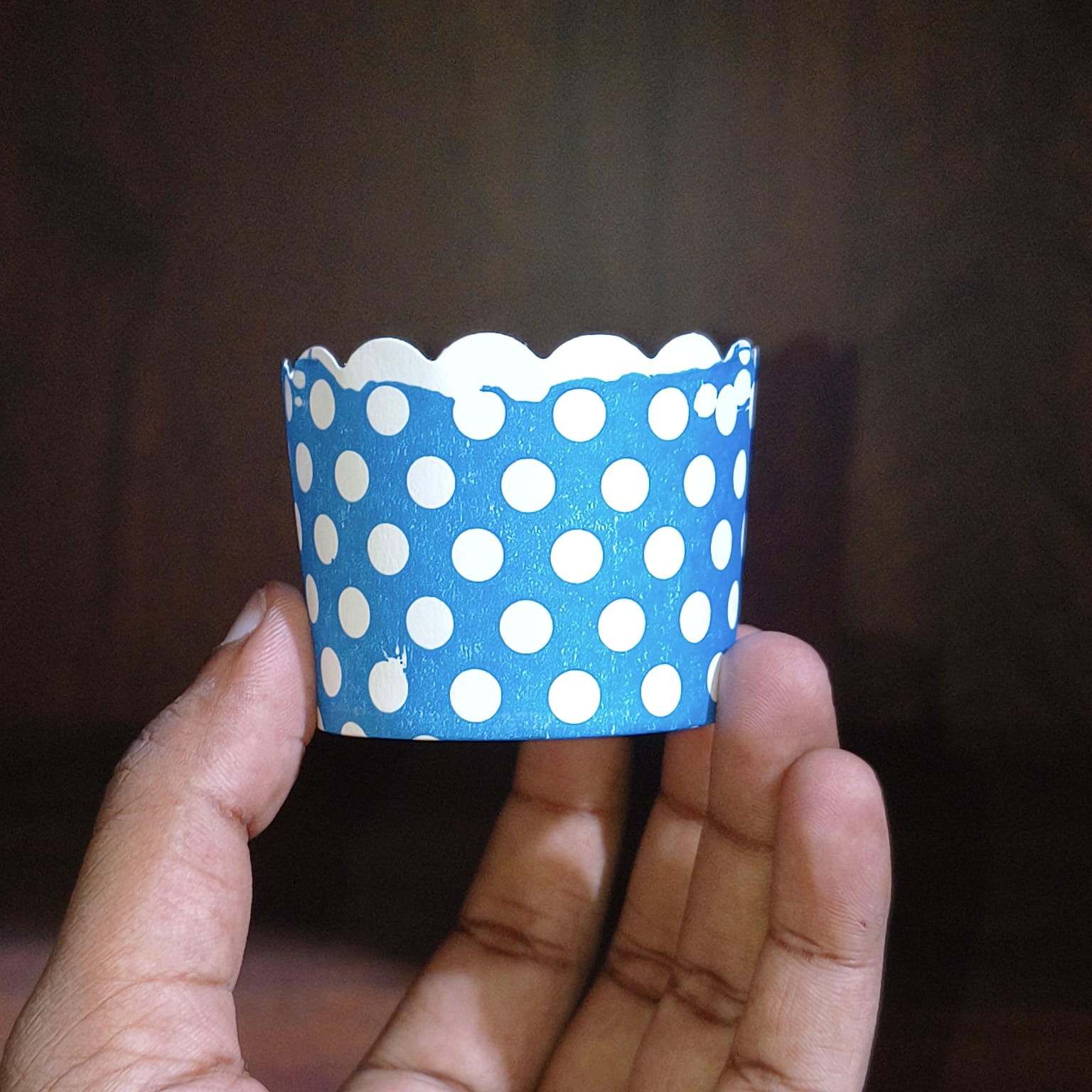 Hand holding a blue paper cup with white polka dots against a dark background
